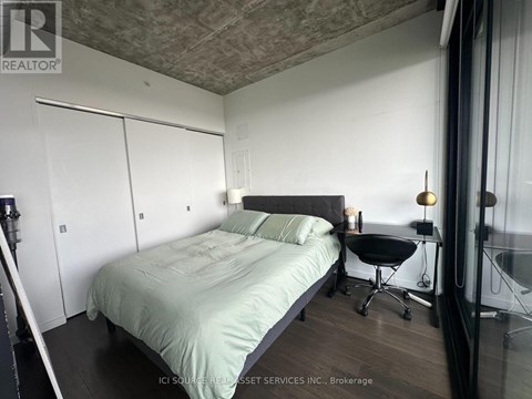 A bedroom with a bed, chair, and a window.