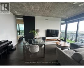 A living room with a grey couch, a glass table, a television, and a piano.