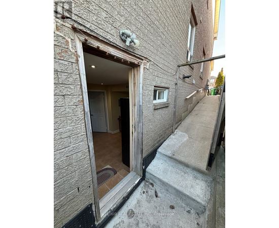 A view of a doorway leading to a room with a brick wall on the left and a concrete staircase on the right.