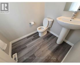 A bathroom with a toilet, sink, and wood flooring.