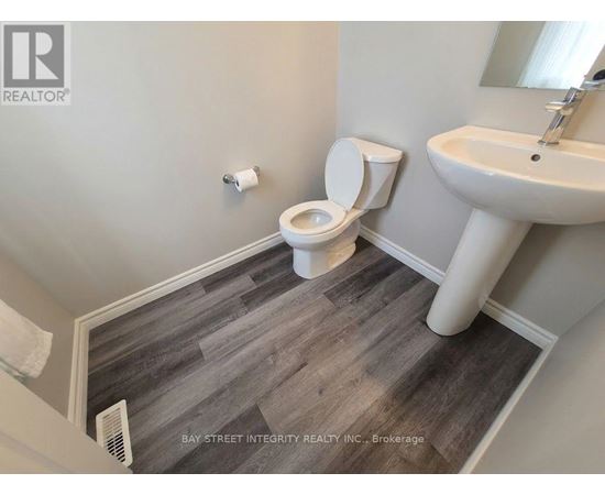 A bathroom with a toilet, sink, and wood flooring.
