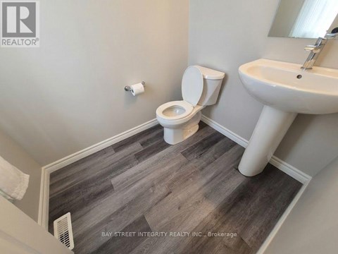 A bathroom with a toilet, sink, and wood flooring.