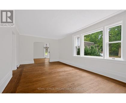 A room with wooden floors and white walls, with a doorway leading to another room.