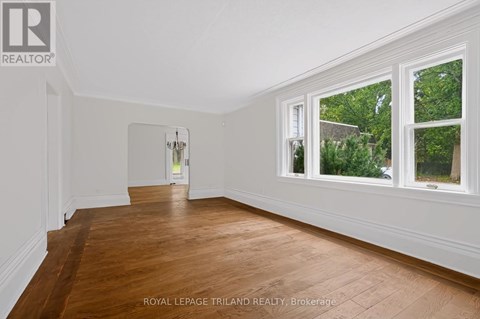 A room with wooden floors and white walls, with a doorway leading to another room.