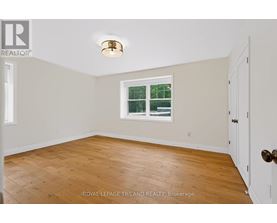 A room with a wooden floor and a window with a view of a fence and trees.