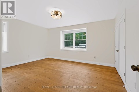 A room with a wooden floor and a window with a view of a fence and trees.