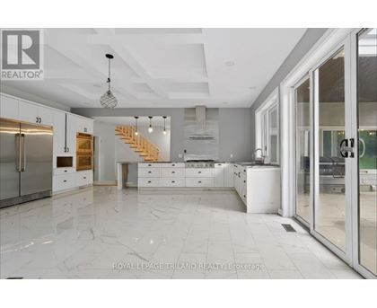 A spacious kitchen with marble flooring and a staircase in the background.