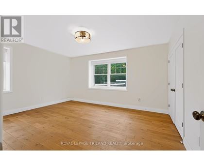 A room with a wooden floor and a window with a view of a fence and trees.