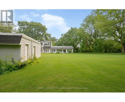 A grassy field with a white house and a tree in the background.