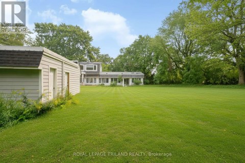A grassy field with a white house and a tree in the background.