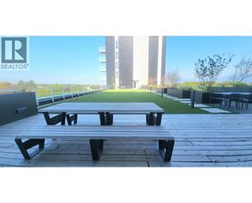 A wooden picnic table is in the foreground of a sunny outdoor area with a building in the background.