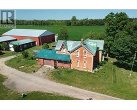 A red brick house with a green roof is surrounded by a grassy field.