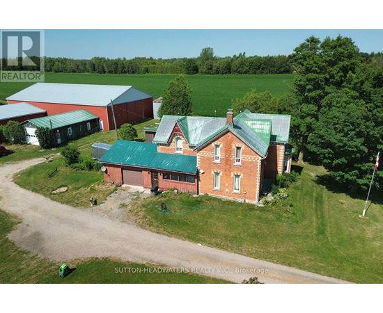 A red brick house with a green roof is surrounded by a grassy field.