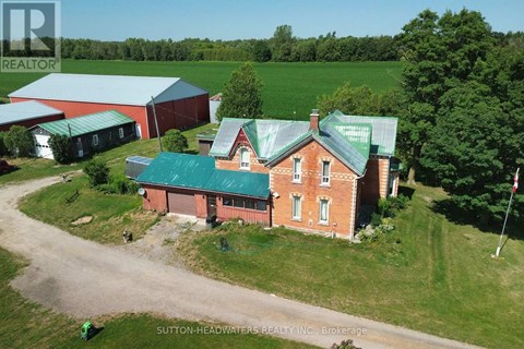 A red brick house with a green roof is surrounded by a grassy field.