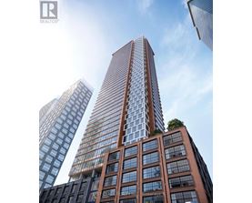 A tall building with a glass facade stands in front of two other buildings.