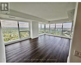 A spacious room with wooden floors and large windows overlooking a cityscape.