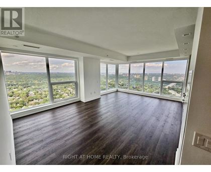 A spacious room with wooden floors and large windows overlooking a cityscape.