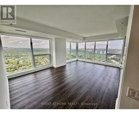 A spacious room with wooden floors and large windows overlooking a cityscape.