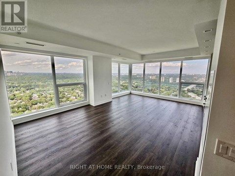 A spacious room with wooden floors and large windows overlooking a cityscape.