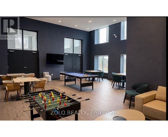 A foosball table is in the middle of a room with a pool table and a couch.