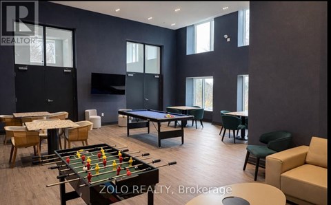 A foosball table is in the middle of a room with a pool table and a couch.