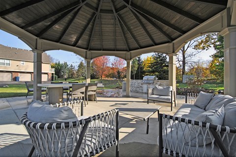 A gazebo with grey couches and a table is surrounded by trees.