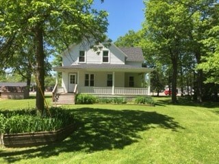 A white house with a grey roof and a porch surrounded by green trees.