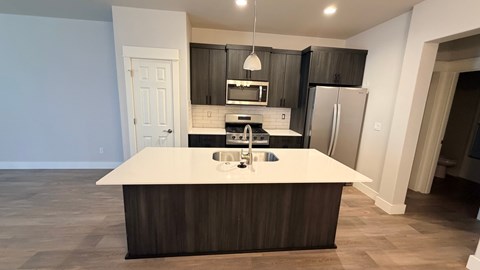 A modern kitchen with a white island and dark wood cabinets.