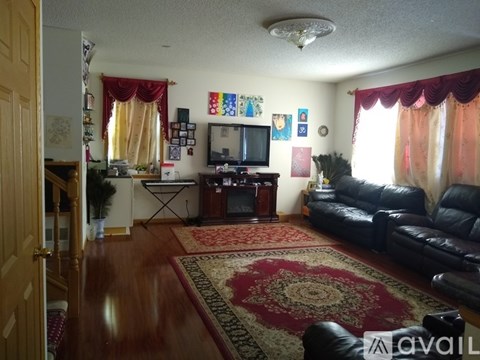 A living room with a black leather couch and a red rug.