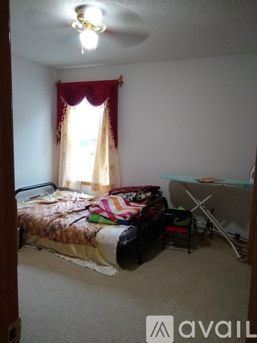 A bedroom with a bed, chair, and window with red curtains.