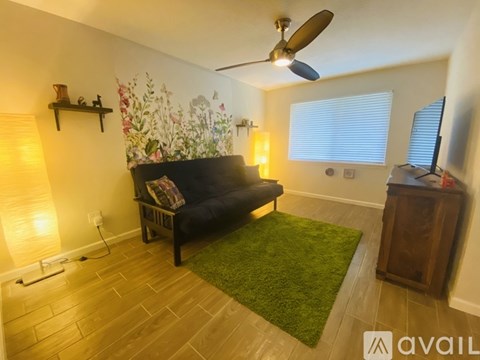 A living room with a black couch, a green rug, and a ceiling fan.