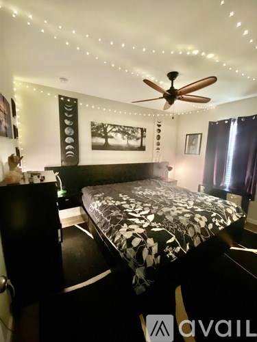 A bedroom with a bed, a ceiling fan, and a wall-mounted picture.