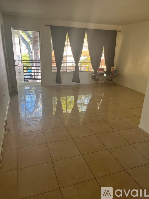 A spacious room with a tiled floor and large windows with curtains.