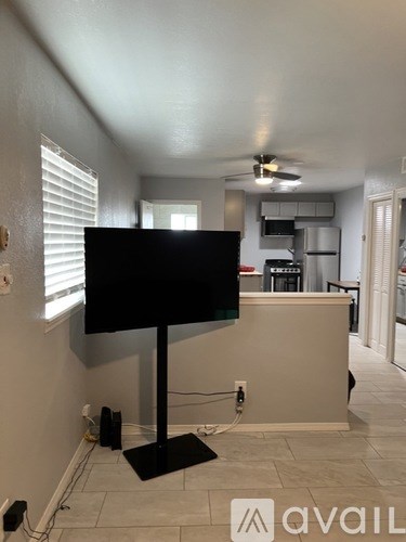 A black television set on a black stand in a room with a ceiling fan.