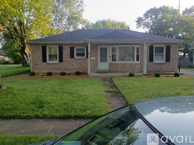 A small house with a grey roof and a white door is surrounded by a green lawn.