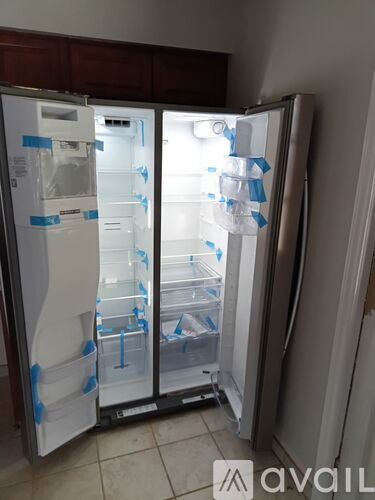 A white refrigerator with the door open and taped in plastic.