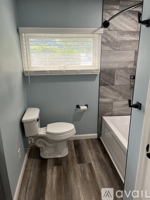 A bathroom with a toilet, a window with blinds, and a shower area.