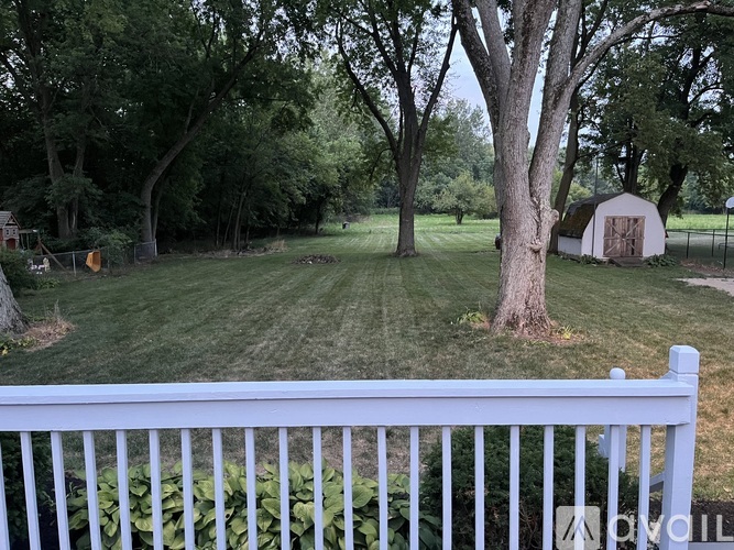 A white fence in front of a grassy field with trees and a small building in the background.