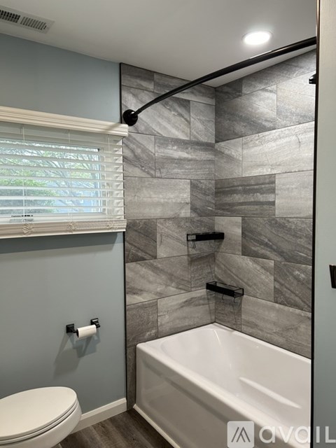 A bathroom with a toilet, a tub, and a window with blinds.