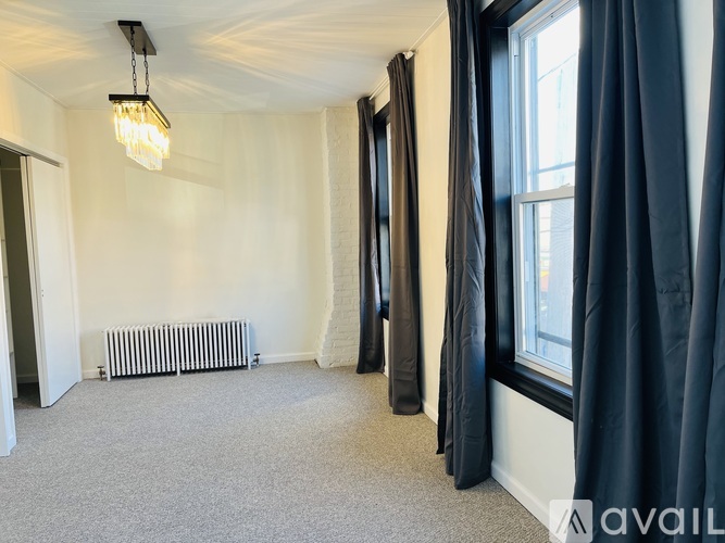 A room with a carpeted floor, a window with black curtains, and a radiator.
