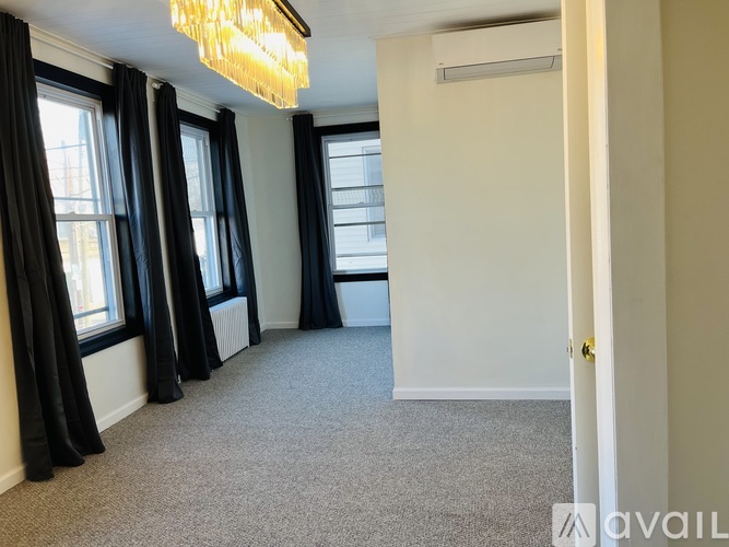 A room with a carpeted floor, a chandelier, and a door on the right.