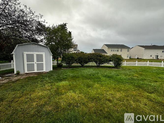 A white shed sits in a grassy field with a house in the background.