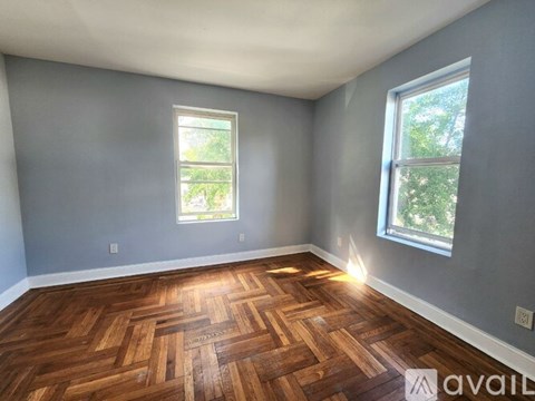 A room with wooden flooring and two windows.