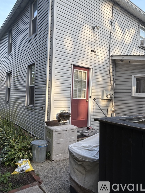 A house with a red door and a trash can in front of it.