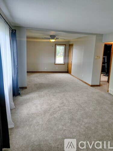 A spacious room with a carpeted floor and a window with a view outside.