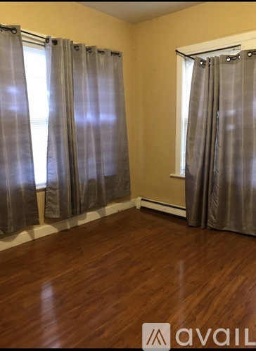 A room with wooden floors and two windows with curtains.