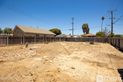 A backyard with a wooden fence and a house in the background.