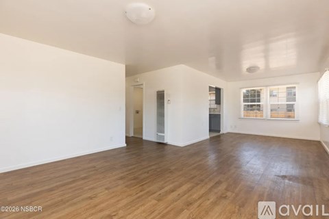 A spacious room with wooden flooring and white walls.