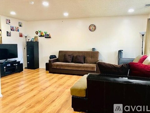 A living room with a brown couch, a black leather couch, and a wooden floor.