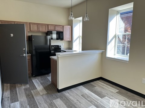 A kitchen with a black fridge and stove, a white counter, and a window with a view of a building outside.